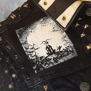 Könnte beinhalten: Schwarze Jeansjacke mit silbernen Nieten und einem weiß-schwarzen gestreiften Kragen. Ein schwarzer Patch mit einem weißen Bild einer Ziegenfigur mit Hörnern und einer Person, die dahinter steht, ist auf die Jacke genäht.