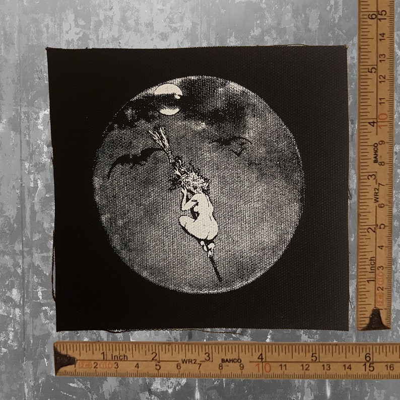 May include: Black and white patch featuring a witch riding a broom against a full moon backdrop. The witch is depicted in a seated position, with bats flying in the sky. The patch is square-shaped.