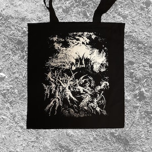 May include: Black tote bag featuring a detailed, monochrome illustration. The artwork depicts a chaotic scene with figures and abstract elements, creating a dark and dramatic aesthetic. The bag has two black handles.