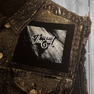 May include: A black denim vest with silver studs and a black patch with white text that says "The End".