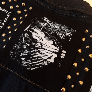 Peut inclure: Veste en jean noire avec un patch blanc représentant une scène de forêt en noir et blanc. La veste est décorée de clous argentés.