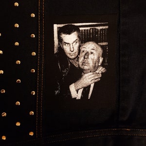 May include: Black and white photo of two men, one with his arm around the other's neck. The man in the back is wearing a dark suit and the man in the front is wearing a light suit. The photo is printed on a black fabric patch.