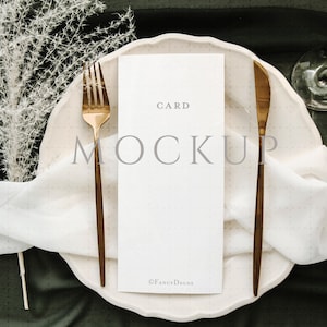 May include: A white card with the text "CARD MOCKUP" on a white plate with gold silverware and a white cloth napkin. The plate is on a dark green surface.