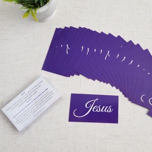 Jesus gospel tracts — Acts 4:12 salvation prayer cards; wide fan spread of purple fronts with sealed 25-pack (back text visible) in clear cellophane, plant décor on linen surface; 25-pack (25–250 options).