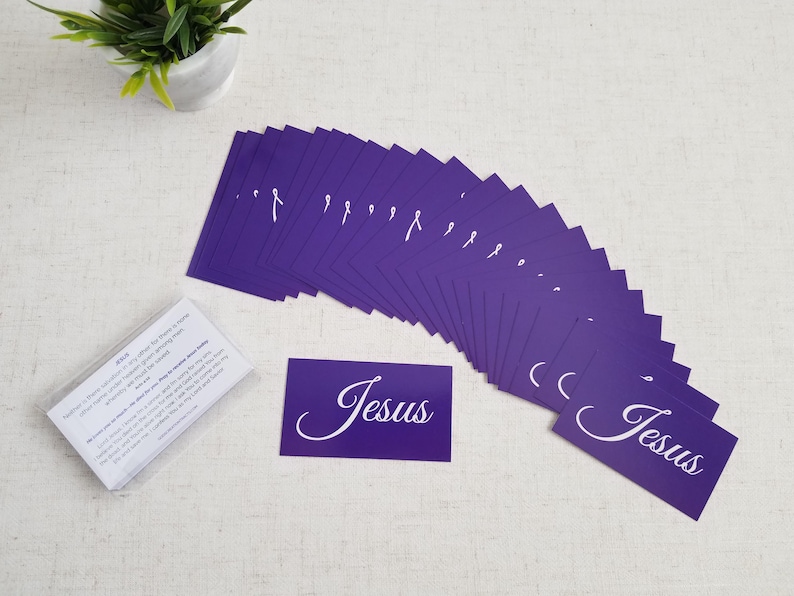 Jesus gospel tracts — Acts 4:12 salvation prayer cards; wide fan spread of purple fronts with sealed 25-pack (back text visible) in clear cellophane, plant décor on linen surface; 25-pack (25–250 options).