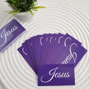 Jesus gospel tracts – Acts 4:12 salvation prayer business cards in purple; fan spread with stacked cards and a sealed 25-pack in a clear resealable cellophane bag, on white round mat with plant décor; Christian evangelism scripture cards