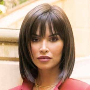 May include: A woman wearing a dark red blazer-style dress with a tie waist and two buttons. She is wearing a layered gold necklace and has a short, dark brown wig with bangs.