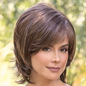 May include: A woman wearing a layered, short brown wig with side-swept bangs. She is wearing a snakeskin print camisole and sunglasses. The background is blurred with green and yellow tones.