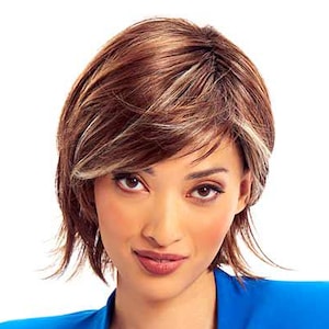 Puede incluir: Una mujer con una peluca corta y en capas con reflejos marrones y rubios. Lleva una blazer azul brillante sobre un top azul a juego. La blazer tiene un corte clásico con solapa de muesca y un bolsillo.