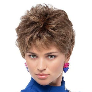 May include: A woman with short, layered, light brown hair and blue earrings. She is wearing a royal blue top with silver buttons. The image is a studio shot with a white background.
