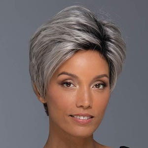 May include: A short, layered wig with a mix of gray and black tones. The wig features a side-swept bang and a natural-looking hairline. The model is wearing a black top against a gray background. The wig is styled to frame the face.