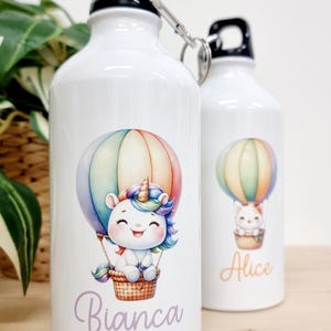 Può includere: Due borracce in alluminio bianco con nomi personalizzati, Bianca e Alice. Ogni borraccia presenta una mongolfiera colorata con un unicorno e un gatto che viaggiano al suo interno.