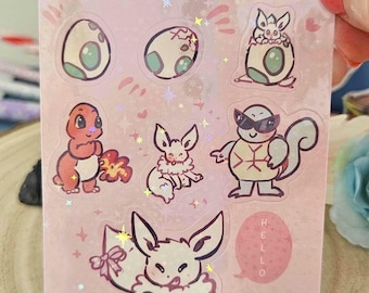May include: A sheet of pink stickers featuring various cartoon characters and egg designs. The stickers include a red creature, a turtle wearing sunglasses, and several bunny-like creatures. The word "HELLO" is on a pink circle.