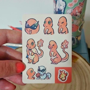 Puede incluir: Una hoja de pegatinas con varios diseños de Charmander de dibujos animados. Las pegatinas representan a Charmander en diferentes poses, algunas con accesorios como gafas de sol y capas. La paleta de colores incluye naranja, azul y blanco.