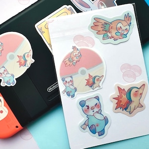 May include: A sheet of stickers featuring various Pokemon characters. The stickers are printed on clear vinyl and have a glossy finish. The characters include a pink and blue Pokemon with a flame tail, a brown and orange Pokemon with wings, and a blue and white Pokemon with a flame tail.