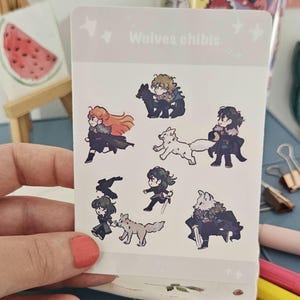 May include: A sticker sheet with chibi-style illustrations of characters and wolves. The stickers have a light grey background with the text "Wolves chibis". The illustrations depict characters in various poses with wolves, in black, white, and grey.