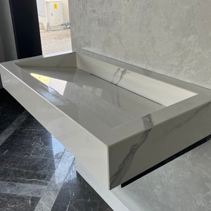 Peut inclure: Un évier rectangulaire en blanc avec un motif marbré. L'évier est monté sur un mur et a une finition lisse et brillante.