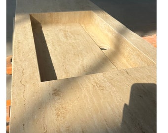 Puede incluir: Una encimera rectangular de piedra travertina beige claro con un lavabo rectangular empotrado. El lavabo tiene un solo agujero de drenaje.