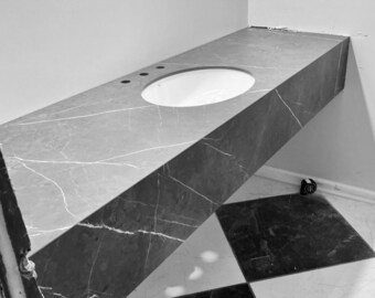 May include: A gray marble countertop with a white oval sink and three faucet holes. The countertop has white veining and is installed in a corner. The floor has a black and white checkered pattern.
