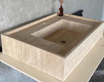 May include: A rectangular stone sink with a square basin and a drain hole. The sink is made of a light beige travertine stone with a textured surface.