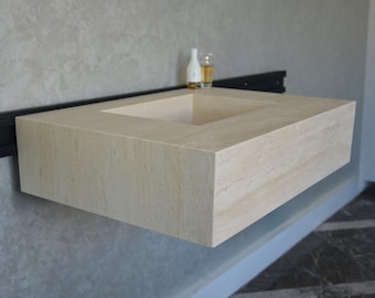 May include: A rectangular stone sink with a square basin, mounted on a wall with a black metal bracket. The sink is made of a light beige stone with visible veins.