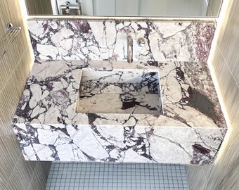 May include: A white marble bathroom vanity with a rectangular sink and a silver faucet. The vanity is mounted on a white tiled wall.