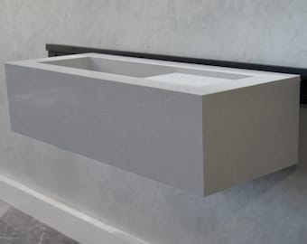May include: A rectangular, light gray, concrete vessel sink with a rectangular cutout for a faucet. The sink is mounted on a wall with a black metal bracket.