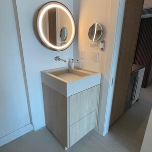 May include: A bathroom vanity featuring a light wood cabinet with two drawers, a rectangular stone sink, and a wall-mounted faucet. Above the sink is a large circular mirror with integrated LED lighting and a smaller adjustable circular mirror.