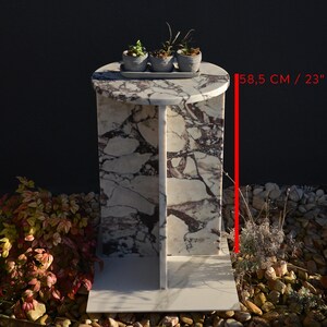 May include: A marble side table with a round top and a rectangular base. The table is 23 inches (58.5 cm) tall and features a white and purple patterned design. Three small potted plants sit on top of the table.
