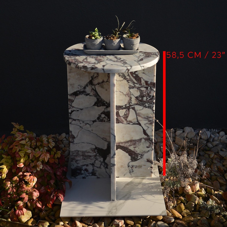 May include: A marble side table with a round top and a rectangular base. The table is 23 inches (58.5 cm) tall and features a white and purple patterned design. Three small potted plants sit on top of the table.