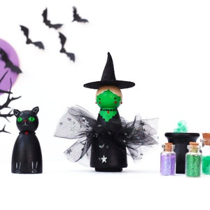 May include: A green witch doll wearing a black hat and dress, a black cat doll, and a cauldron with green glitter. There are also four small bottles with different coloured glitter.