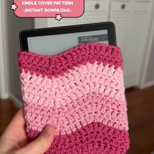 May include: A handmade crochet Kindle cover in shades of pink. The cover features a ripple stitch design and is designed to protect the e-reader. Text on the image reads: "RIPPLE STITCH CROCHET KINDLE COVER PATTERN -INSTANT DOWNLOAD-"