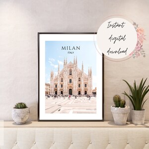 May include: A printable digital download of a photograph of the Duomo di Milano, a large cathedral in Milan, Italy. The image is in a black frame and is displayed on a shelf with plants.