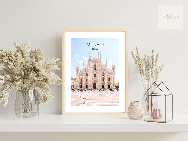 May include: A framed print of the Duomo di Milano, a large cathedral in Milan, Italy. The print features a photo of the cathedral with a blue sky and white clouds in the background. The text "MILAN ITALY" is printed at the top of the print.