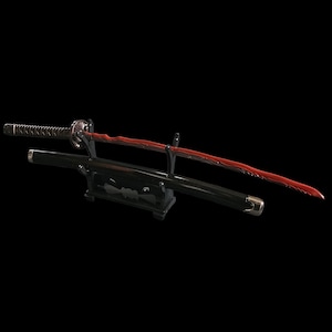 May include: A Japanese katana sword with a red blade and black handle and scabbard. The sword is displayed on a black stand against a black background. The blade has a unique wavy design.
