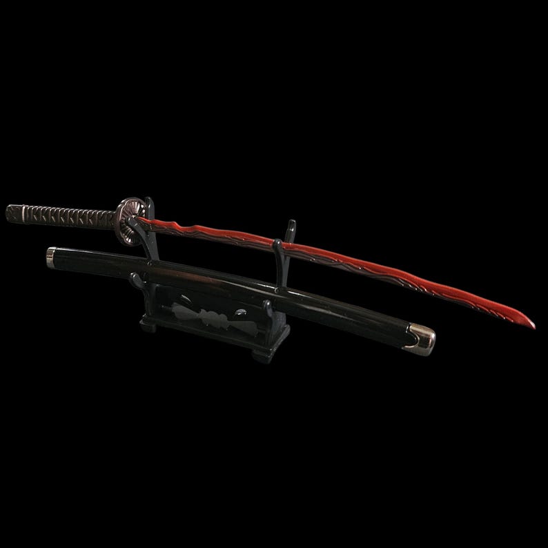 May include: A Japanese katana sword with a red blade and black handle and scabbard. The sword is displayed on a black stand against a black background. The blade has a unique wavy design.