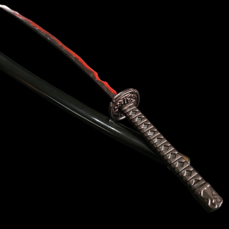 May include: A detailed image of a katana sword with a black scabbard. The blade has a red edge, and the handle is intricately designed with a silver finish. The sword is set against a black background.
