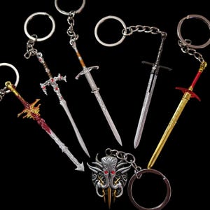 Può includere: Un set di sette portachiavi a forma di spada argentati e rossi con dettagli intricati. I portachiavi presentano diversi modelli di spade, tra cui una spada curva, una spada dritta e una spada con una testa di drago. I portachiavi sono attaccati ad anelli argentati.