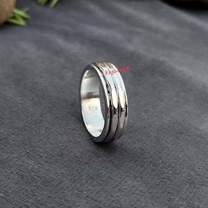 Puede incluir: Un anillo de plata con un diseño texturizado. El anillo tiene un acabado pulido y una banda con un patrón acanalado. El anillo está marcado con "925".