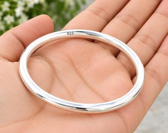 May include: A polished sterling silver bangle bracelet with a smooth, rounded profile. The inner surface of the metal band features the engraved hallmark 925, indicating the silver purity of the jewelry piece.