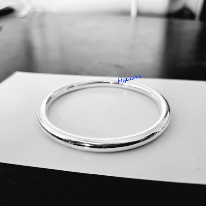 May include: A silver-colored, circular bracelet with a smooth, polished surface. The bracelet is resting on a white surface. The word "kivaluxe" is written in blue in the upper right corner.