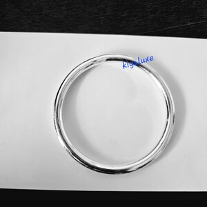 May include: A silver-colored ring with a smooth, reflective surface. The ring is circular and appears to be made of metal. The text "kig luxe" is visible in the image.