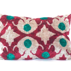 Peut inclure: Un coussin rectangulaire avec un motif géométrique rouge, blanc et vert. Le coussin est fait d'un tissu doux et velouté.
