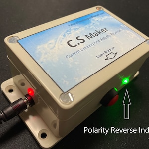 May include: A beige electronic device labeled "C.S. Maker" with "Current Limiting and Polarity Reverse" text. It has a red and green LED indicator, a black and red button, and a power input. The text "Polarity Reverse Indicator" is also visible.