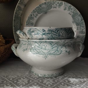 Peut inclure: Ensemble de plats de service anciens en céramique blanche avec un motif floral et de moulin à vent turquoise. L'ensemble comprend une grande soupière, un bol et deux assiettes, le tout empilé sur une nappe en dentelle blanche.