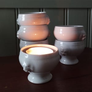 Peut inclure: Ensemble de cinq bols en céramique blanche avec un motif de tête de lion décoratif. Les bols sont empilés les uns sur les autres, avec une bougie chauffe-plat dans le bol du haut.