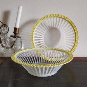 Op de afbeelding: Een witte en gele keramische serveerschaal en bordenset. De kom heeft een geschulpte gele rand en verticale witte spijlen. Het bord heeft een vergelijkbaar ontwerp. De set staat op een donker houten oppervlak.