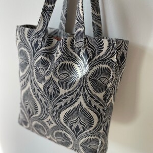 K&ouml;nnte beinhalten: Eine schwarze und wei&szlig;e Einkaufstasche mit einem Blumenmuster. Die Tasche hat zwei Henkel und ist aus robustem Stoff.