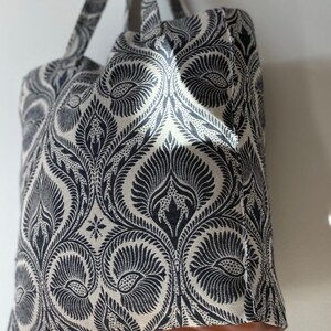 K&ouml;nnte beinhalten: Eine gro&szlig;e Tragetasche mit einem schwarzen und wei&szlig;en Paisley-Muster. Die Tasche hat braune Ledergriffe und einen braunen Lederboden.