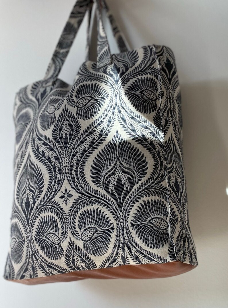 K&ouml;nnte beinhalten: Eine gro&szlig;e Tragetasche mit einem schwarzen und wei&szlig;en Paisley-Muster. Die Tasche hat braune Ledergriffe und einen braunen Lederboden.